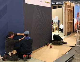 Zwei Mitarbeiter bearbeiten die Oberfläche einer Ausstellungswand.