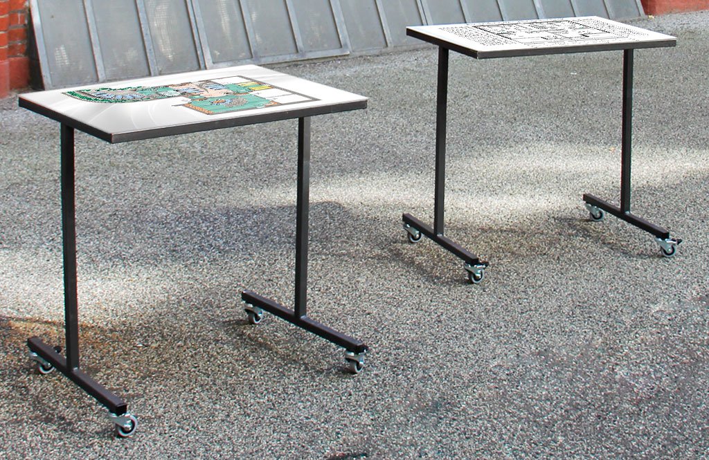 Zwei Architekturmodelltische auf Rollen in einer Ausstellungssituation. Darauf sind Grafiken zu sehen.